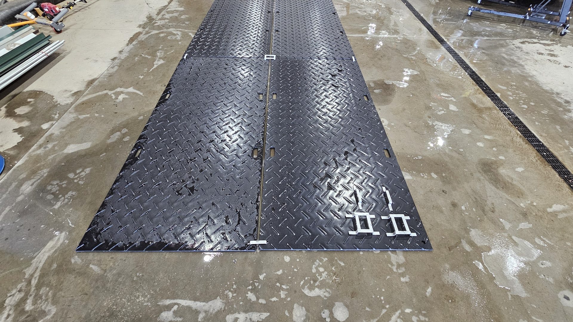 Black HDPE ground mats laid out with metal connectors in warehouse